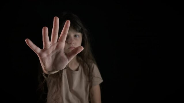 Kid show stop gesture on black. A young girl with stressed angry emotions show stop gesture on the black background.