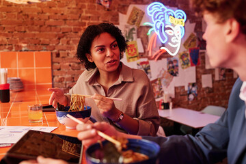 Pretty woman looking at male colleague or her boyfriend at lunch break or date while sitting in front of him and explaining something during chat