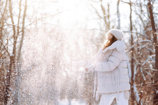 Young woman enjoys the wonderful winter atmosphere in the forest. Woman standing among snowy trees and enjoying first snow. Happy winter time.