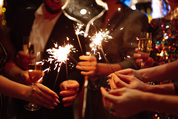 Glowing sparkles in hands. Group of happy people enjoying party with fireworks. Winter holiday. 