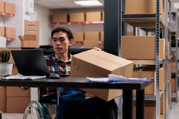 Asian wheelchair user managing parcel delivery in postal service warehouse. Storehouse shipment...