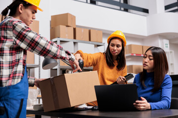 Asian package handler and delivery operators preparing parcel for shipment. Post office warehouse employees coworkers using barcode scanner and checking customer order on laptop