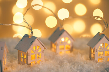 Fototapeta na wymiar Wooden houses garland string lights on snow and glowing lights bokeh background. Christmas, New Year greeting card with copy space. Holiday illumination, home decor.