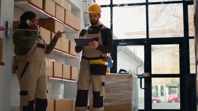 Chief supply chain officer and employee preparing warehouse orders for delivery, receiving phone call in depot while scanning labels on cardboard boxes parcels to be shipped