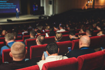 Audience at the modern conference hall listens to panel discussion, people on a congress together listen to speaker on stage at convention, business seminar, amphitheater venue for presentation