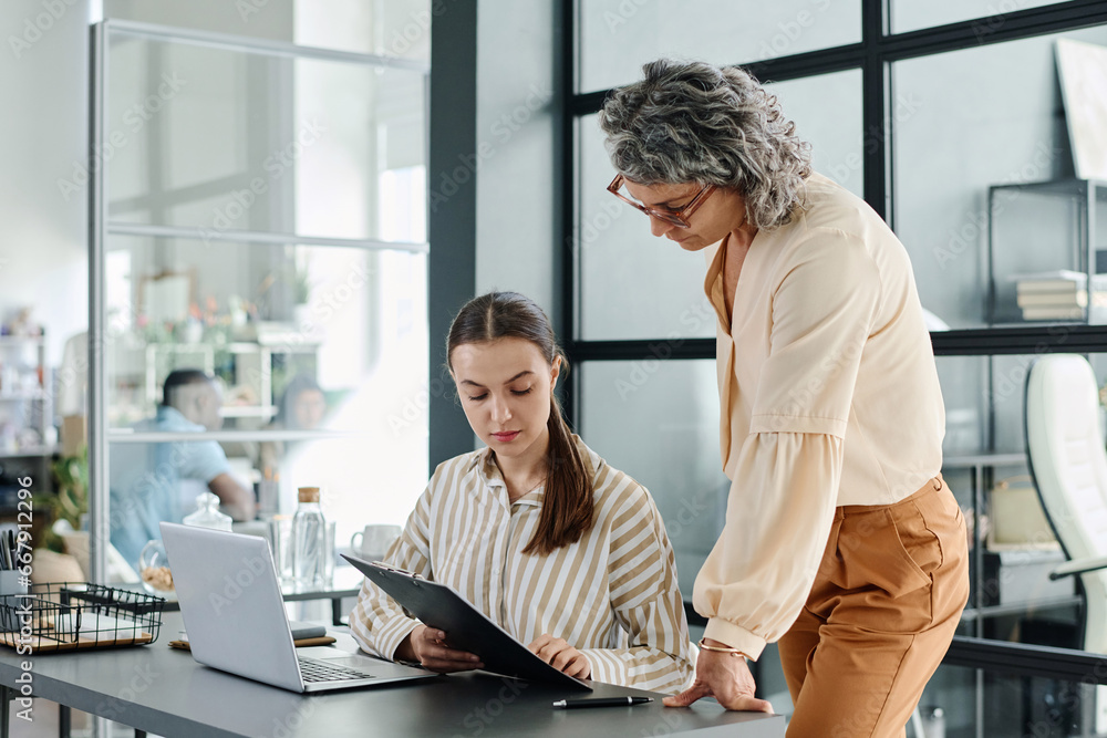 Poster young businesswoman with document consulting with her boss about points of contract while preparing 