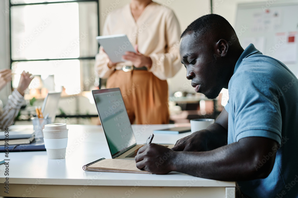Leinwandbilder side view of young african american businessman making notes in notepad while sitting in front of ca