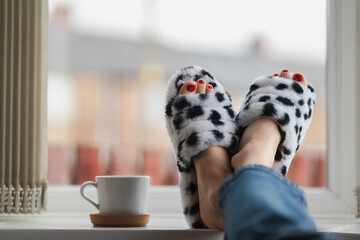 Female legs wearing funny home slippers relaxing near the window