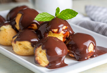 Delicious profiteroles with chocolate and white plate. Selective focus image on light background.
