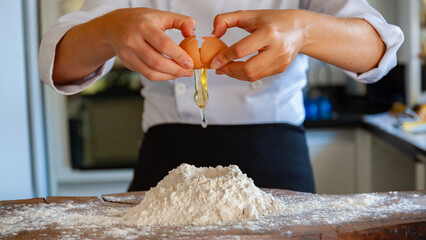 Hand of a female chef, breaking in wheat flour to prepare pizza dough, gnocchi or bread on wooden countertop