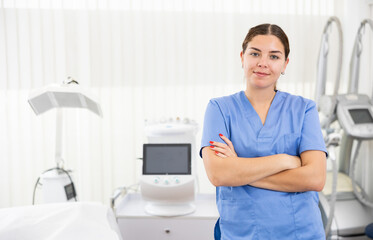 Portrait of young confident professional female beautician in uniform at her workplace in modern beauty spa salon