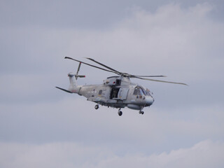 Ein grauer Hubschrauber der englischen Küstenwache fliegt mit geöffneter Tür am Himmel vor der englischen Küste bei Falmouth England