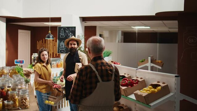 Vendor assisting client interrupted by his partner farmer arriving in eco friendly supermarket to deliver organic food order. Senior trader brings healthy vegetables to local neighborhood grocery shop