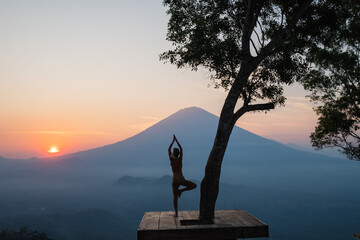 Silhouette of a girl practicing yoga in nature, with a stunning view of the Agung volcano, on the island of Bali, in the sunset rays of the sun.