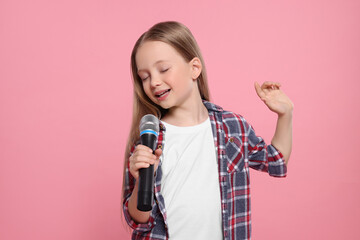 Cute little girl with microphone singing on pink background