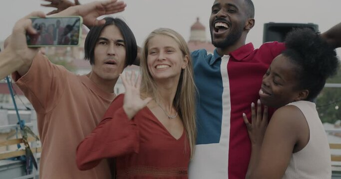 Slow motion of happy young people friends posing for smartphone camera dancing and laughing on rooftop. Friendship and entertainment concept.