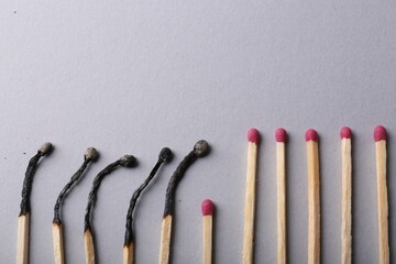 Burnt and whole matches on light grey background, flat lay. Space for text