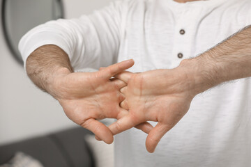 Man cracking his knuckles on blurred background, closeup. Bad habit