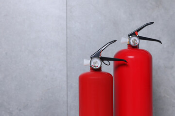 Fire extinguishers near grey wall, space for text