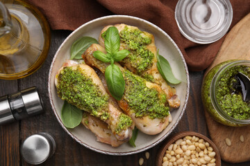 Delicious fried chicken drumsticks with pesto sauce and ingredients on wooden table, flat lay