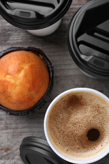Coffee to go. Paper cups with tasty drink and muffin on wooden table, flat lay
