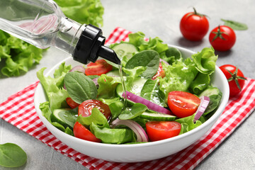 Pouring oil into delicious vegetable salad on light grey table, closeup