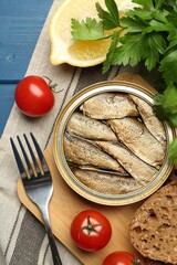 Tin can with tasty sprats served on blue wooden table, flat lay