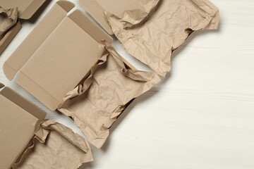 Open cardboard boxes with crumpled paper on white wooden floor, flat lay. Space for text
