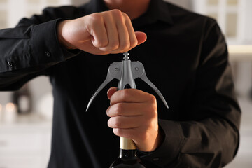 Man opening wine bottle with corkscrew indoors, closeup