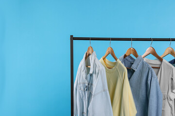 Rack with stylish clothes on wooden hangers against light blue background, space for text