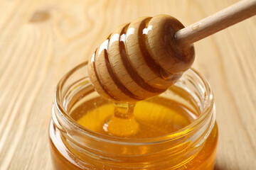 Pouring honey from dipper into jar on wooden table, closeup