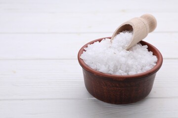 Bowl and scoop with sea salt on white wooden table, closeup. Space for text