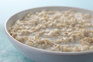 Tasty boiled oatmeal in bowl on light blue table, closeup