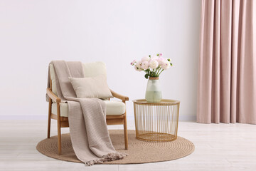 Comfortable armchair with blanket, pillow, table and beautiful flowers in room