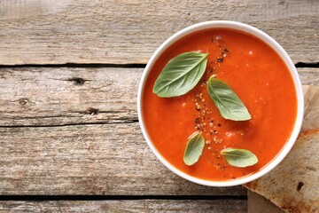 Delicious tomato soup with basil and spices on wooden table, top view. Space for text