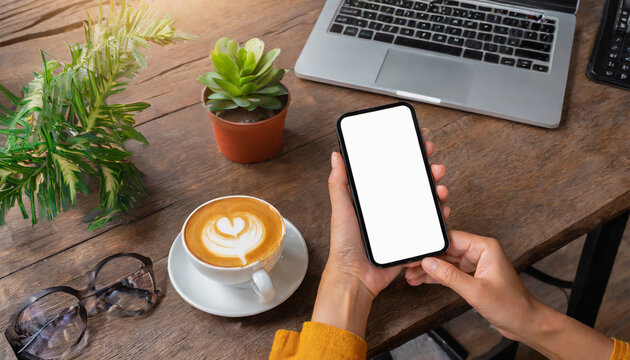 hand holding and using a smartphone with blank desktop screen while working and drinking coffee in cafe. Mockup mobile phone.