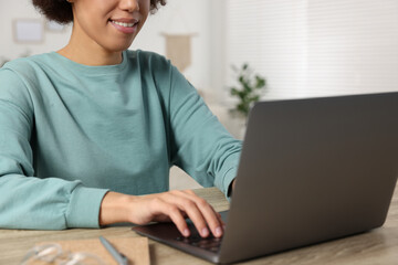 Young woman using laptop at wooden desk in room, closeup
