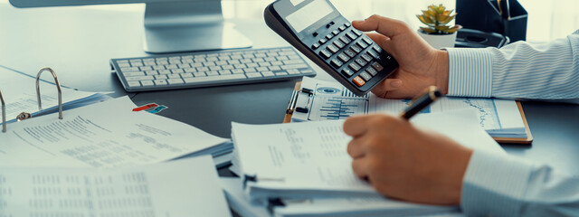 Corporate auditor calculating budget with calculator on his office desk. Dedicated accountant professional of accounting business company analyzing financial document to forecast income. Insight - obrazy, fototapety, plakaty