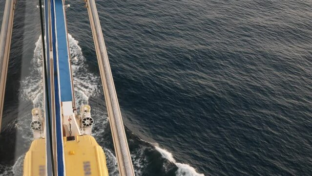 Lifeboat on giant cruise ship view down to ocean surface with waves below while ship cruising saling in the sea. safety muster lifeboat equipment.