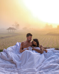 sunrise over rice paddies in Nan Thailand, man and woman in outdoor bed with coffee in the morning