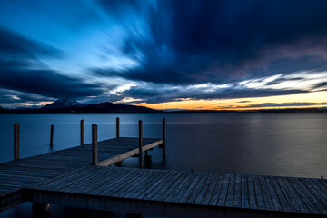 Holzsteg am Seeufers vom Zugersee, Schweiz, bei Abendstimmung, dunklen Wolken und Sonnenuntergang...