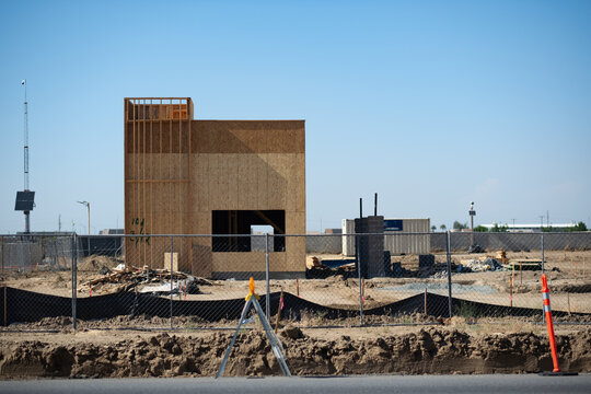 A fenced-off construction site has the ground cleared, and a fast food location rises up, built out of wood framing and plywood. Located in the San Joaquin Valley, it highlights development there.