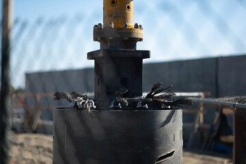 A massive drill bit is positioned against the earth at a major construction site for a statewide infrastructure project. The big dill is used to prepare foundation pilings that go deep underground.