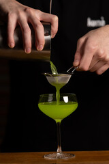 A bartender's hands seen making a green cocktail.