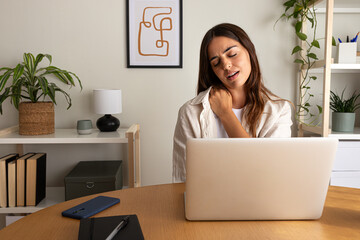 Woman with neck pain after working with laptop. Female self massaging neck and shoulders at home office. Copy space. - obrazy, fototapety, plakaty