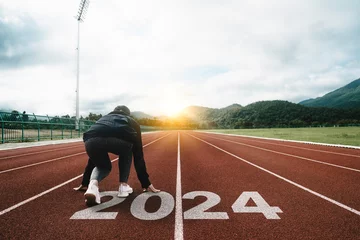 Foto op Plexiglas Happy New Year 2024 symbolizes the start of the new year. Woman preparing to run on the athletics track is engraved with the year 2024. start challenge goal of planning health and business to success © Deemerwha studio