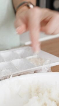 Vertical video. The Woman Places the Coconut Shreds into a Plastic Ice Tray, she is preparing sweet coconut candies.