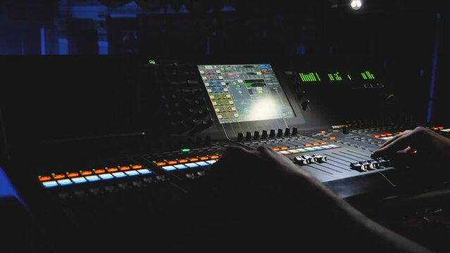 A sound engineer is moving levers and pressing buttons on a multitrack mixing console. The sound engineer's work at a concert. Control parameters are displayed on LED screen