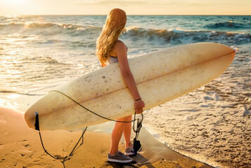 Pretty young woman and her surfboard at sunset - 667986872