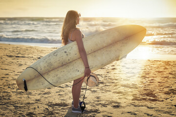 Pretty young woman and her surfboard at sunset - obrazy, fototapety, plakaty